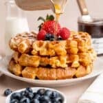 Pouring maple syrup on top of a stack of waffles.
