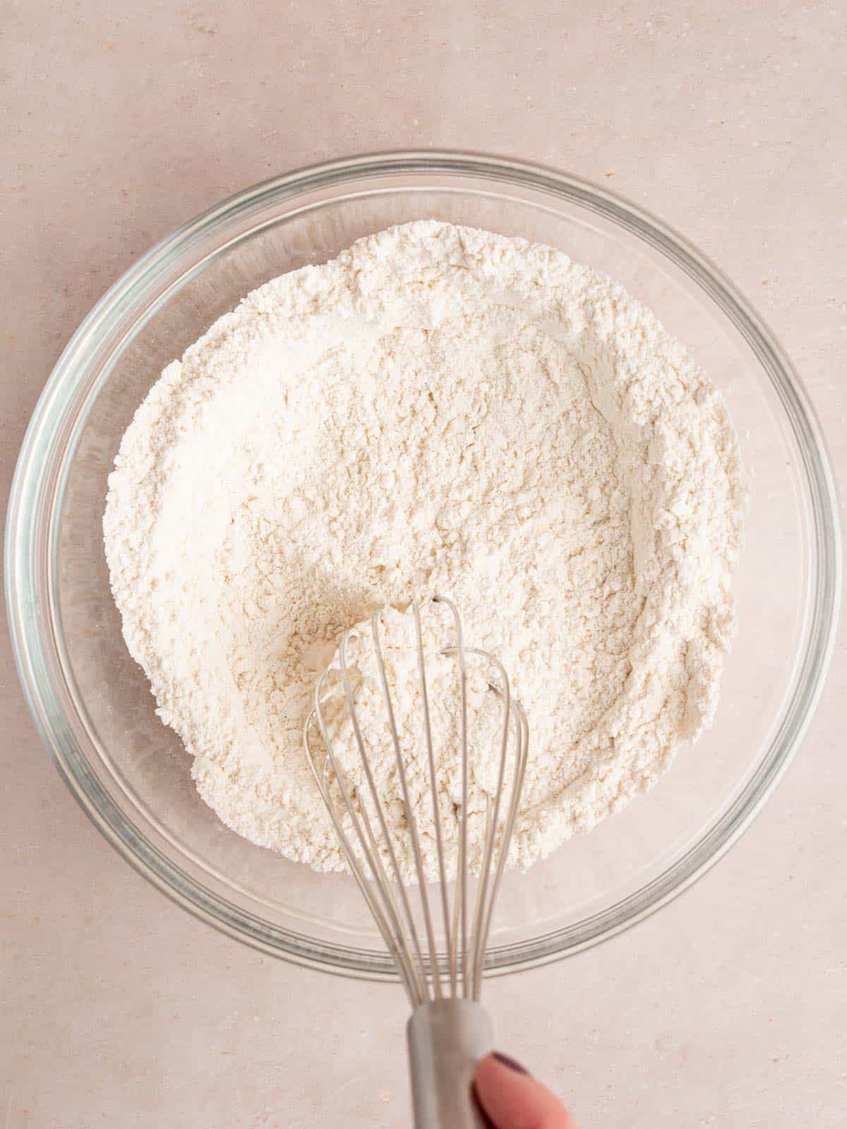 Whisking flour, baking powder, baking soda, sugar, and salt in a bowl.