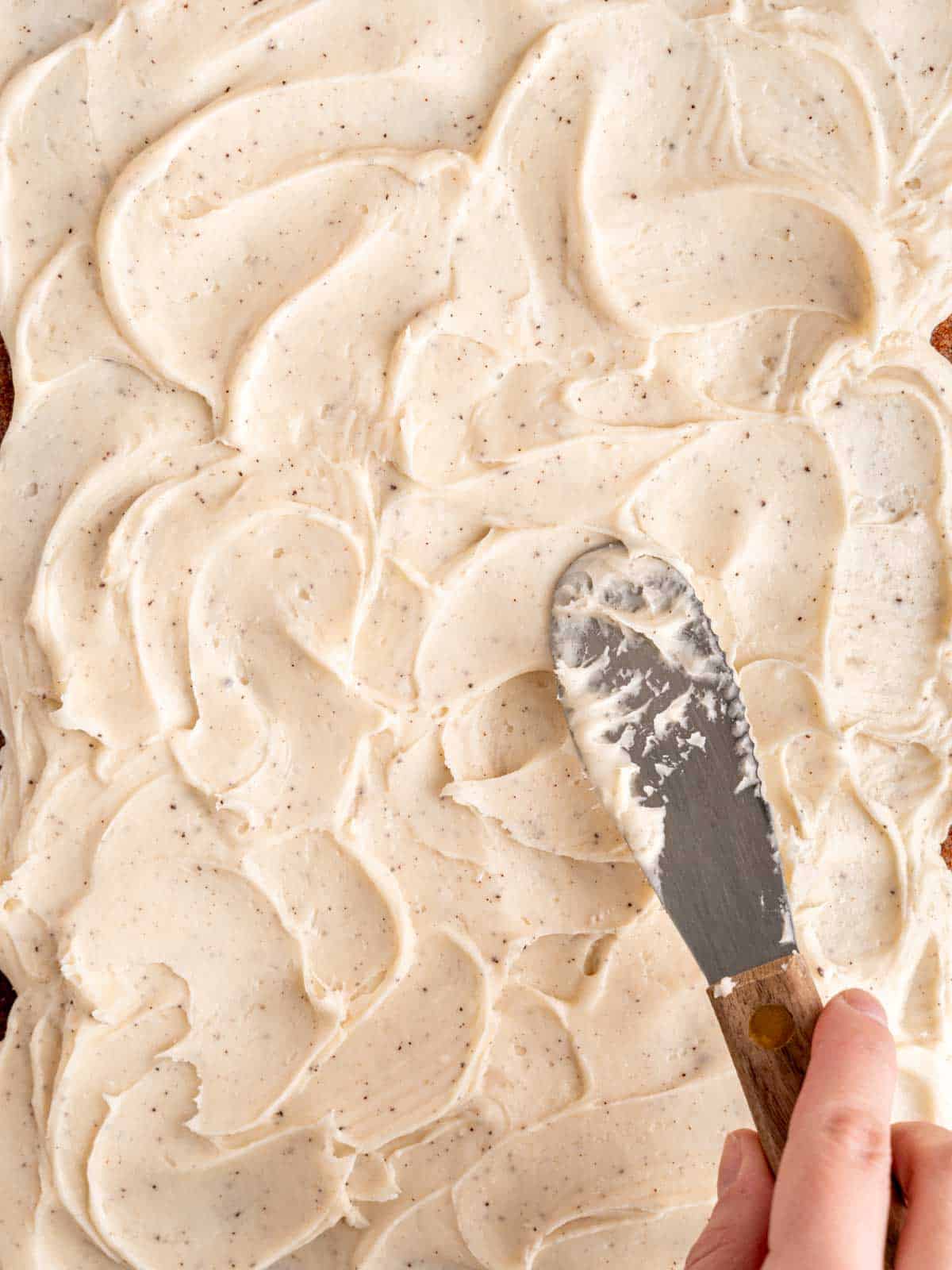 Spreading brown butter cream cheese frosting on top of a spiced carrot sheet cake.