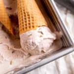 A cone with a scoop of lavender honey ice cream laying in a pan of ice cream.