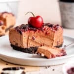 A slice of creamy no bake chocolate cherry cheesecake on a plate with a bite taken out.