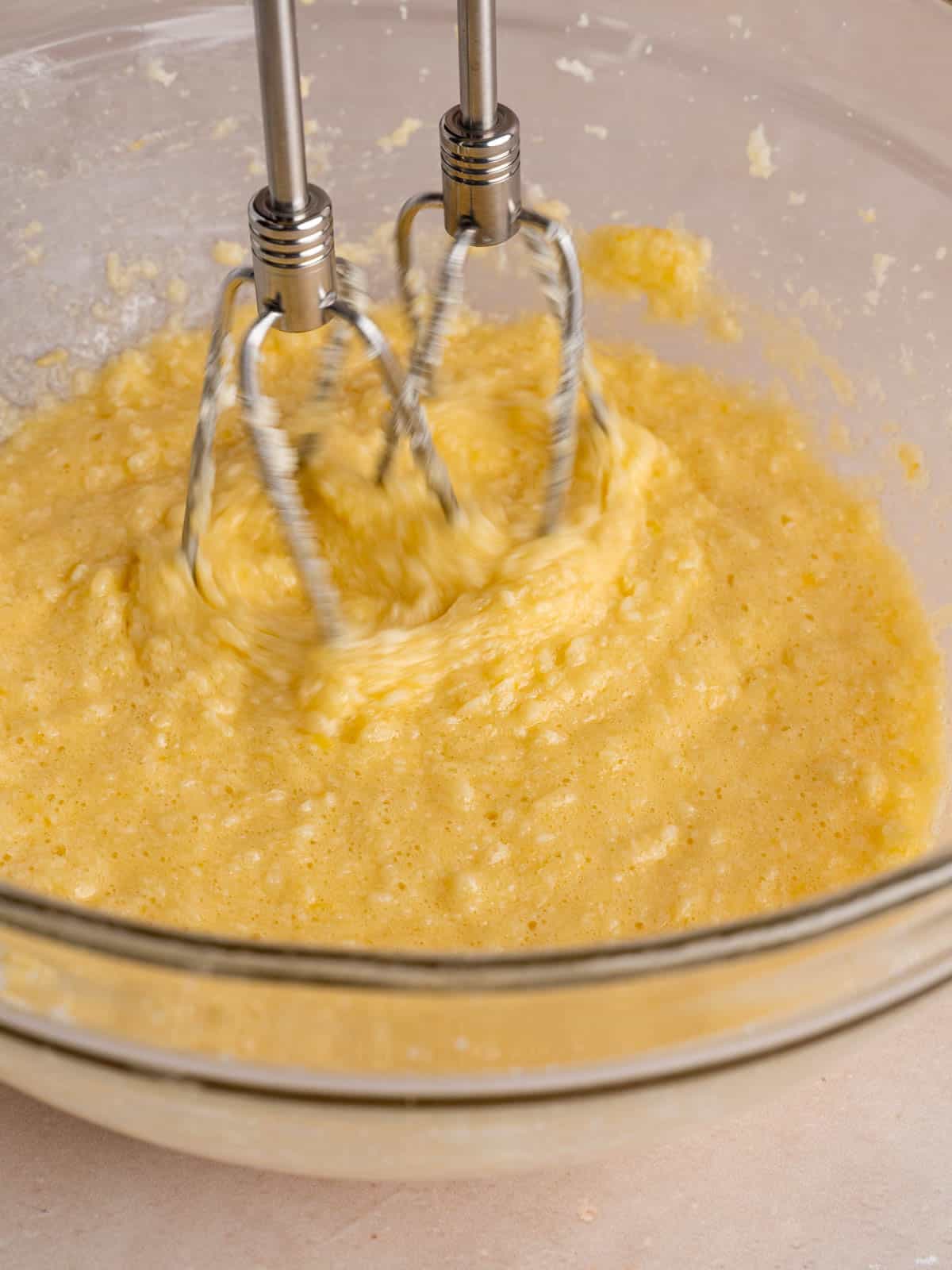 Mixing butter, sugar, lemon zest, eggs, and vanilla extract in a bowl with a hand mixer.