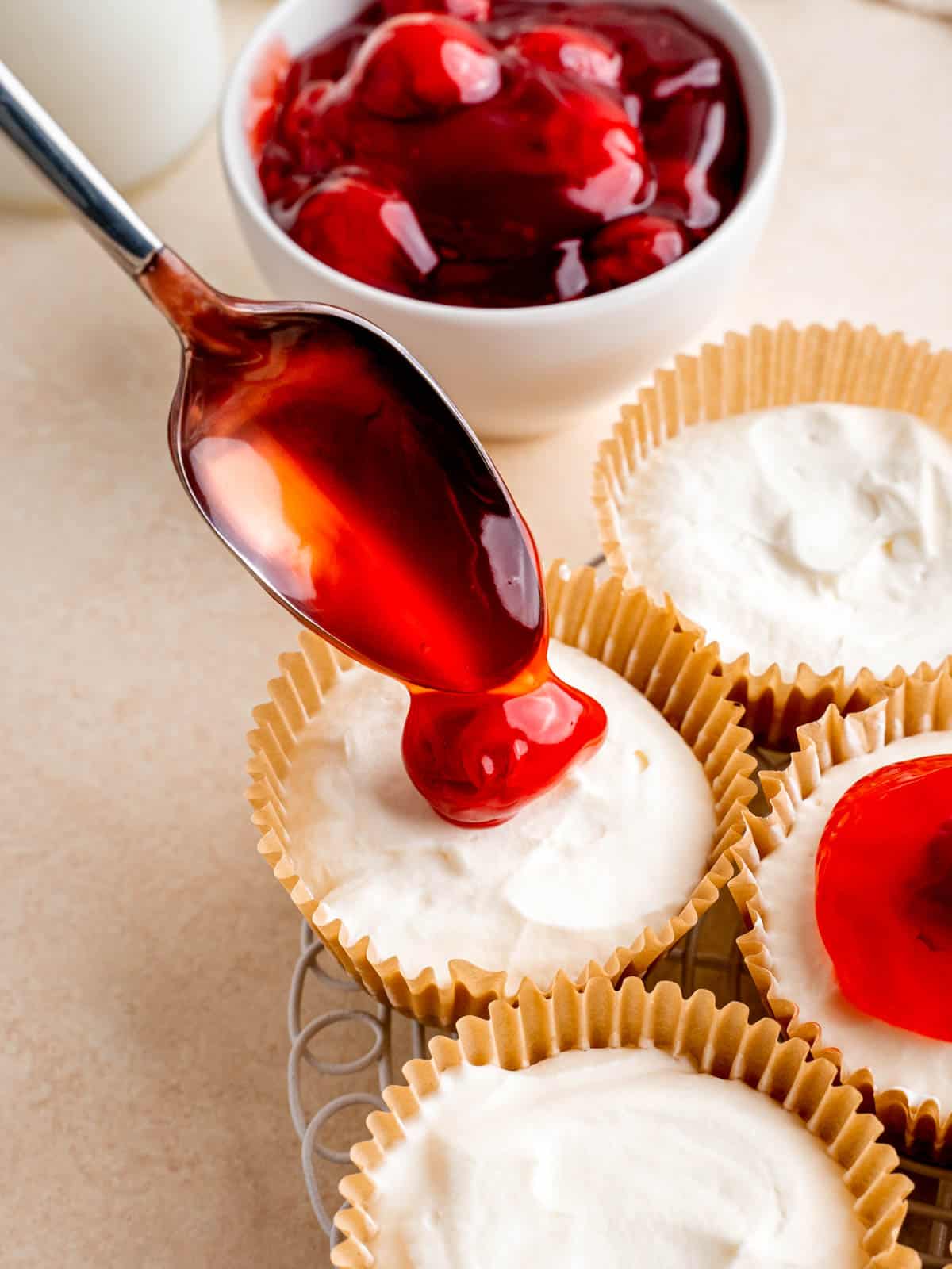 Adding cherry pie filling to the top of a no-bake mini cheesecake.