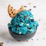 Scoops of edible cookie monster cookie dough with a chocolate chip cookie in a bowl.