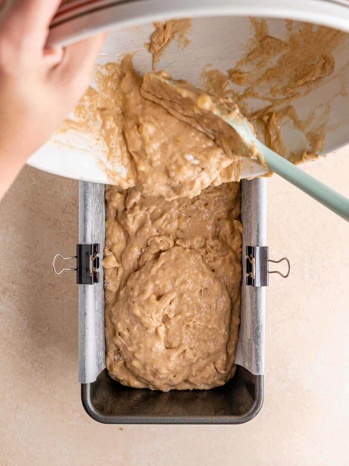 Pouring sourdough discard banana bread batter into a loaf pan lined with parchment paper.