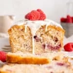 A raspberry white chocolate loaf cake with white chocolate and raspberries on top.