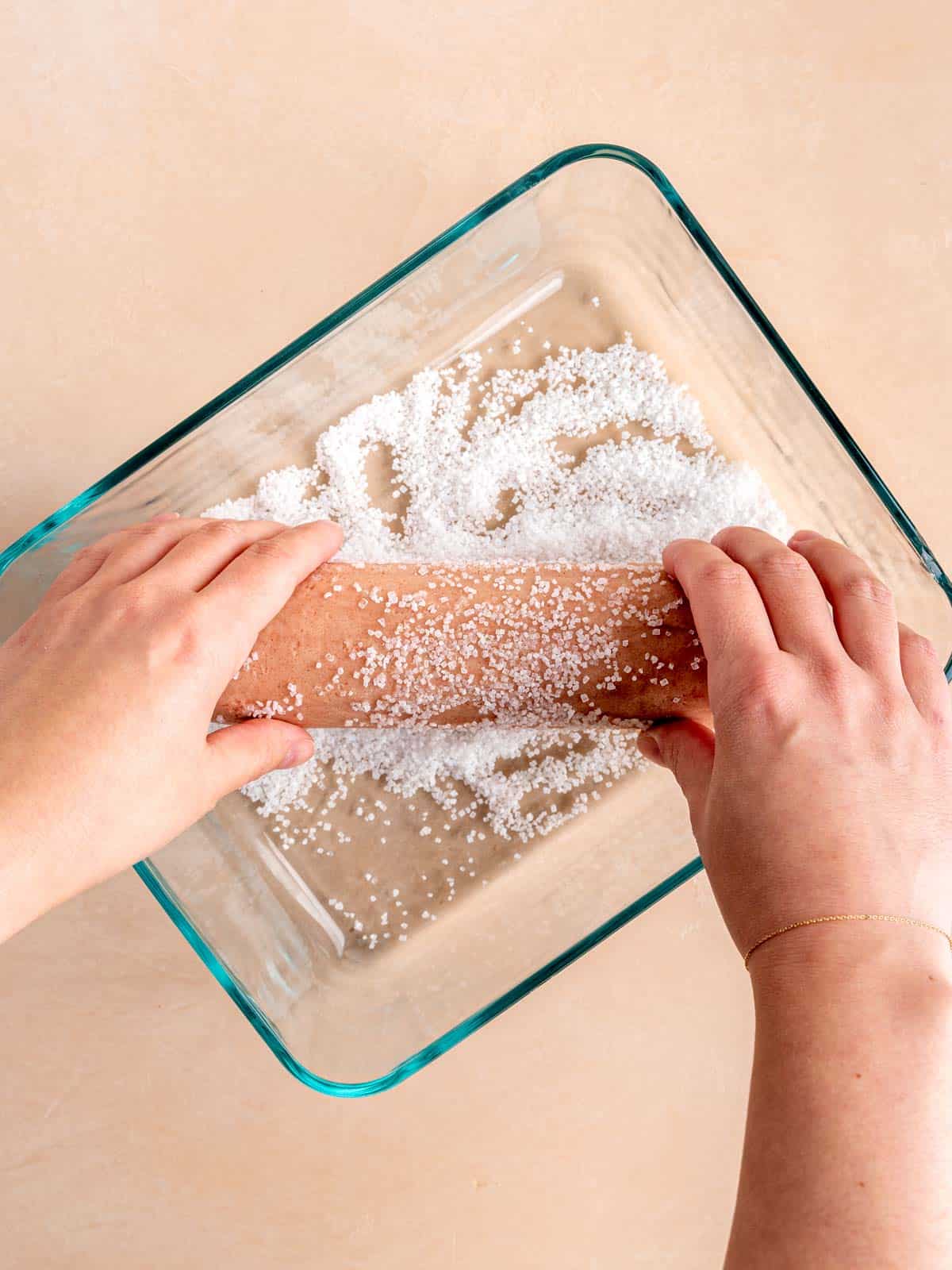 Hands rolling a log of strawberry shortbread cookie dough in sparkling sugar.