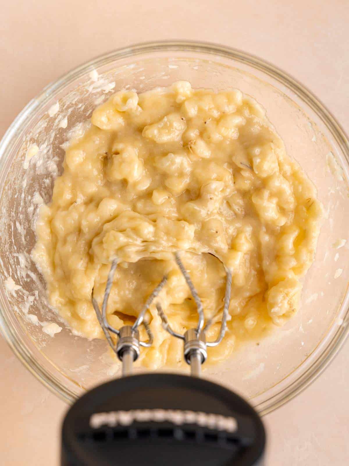 Mashing bananas in a bowl with a Kitchenaid cordless hand mixer.