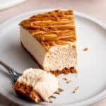A slice of no bake Biscoff cheesecake drizzled in cookie butter on a plate with a bite taken out of it.