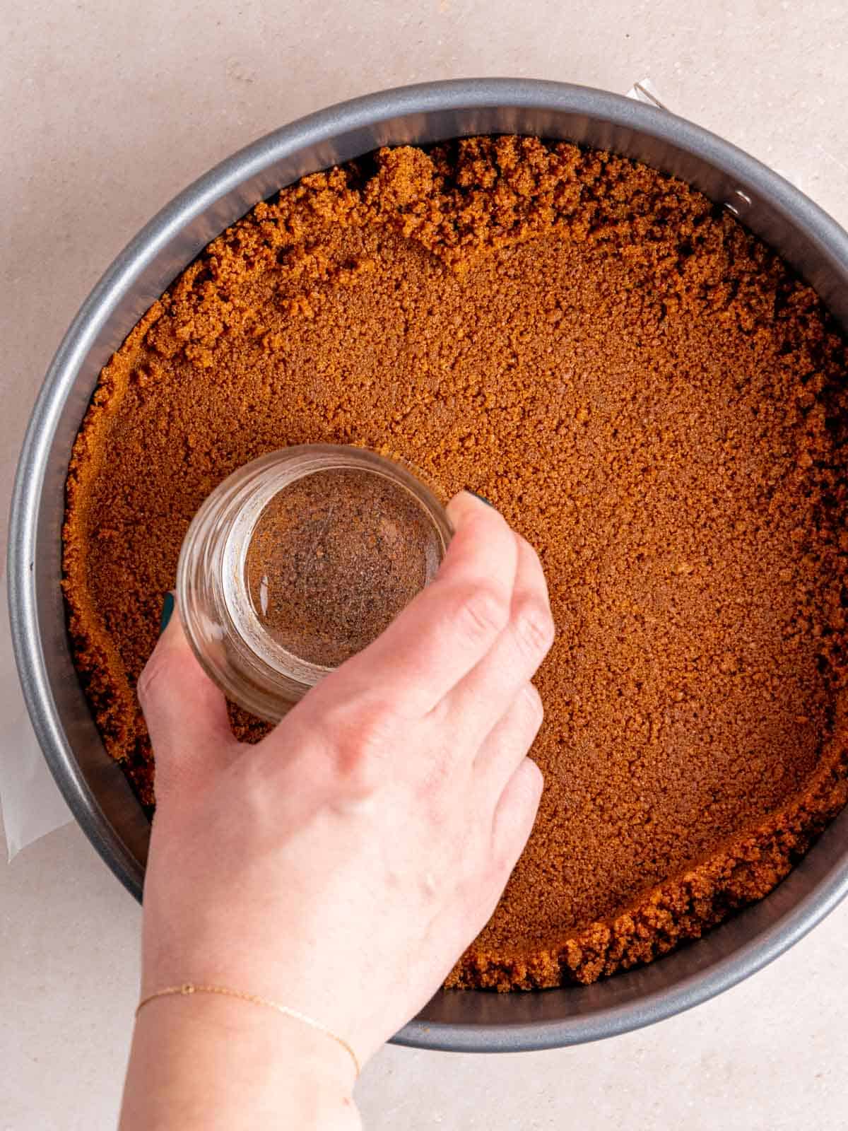 Pressing Biscoff cookie crumbs into a springform pan with the bottom of a glass.
