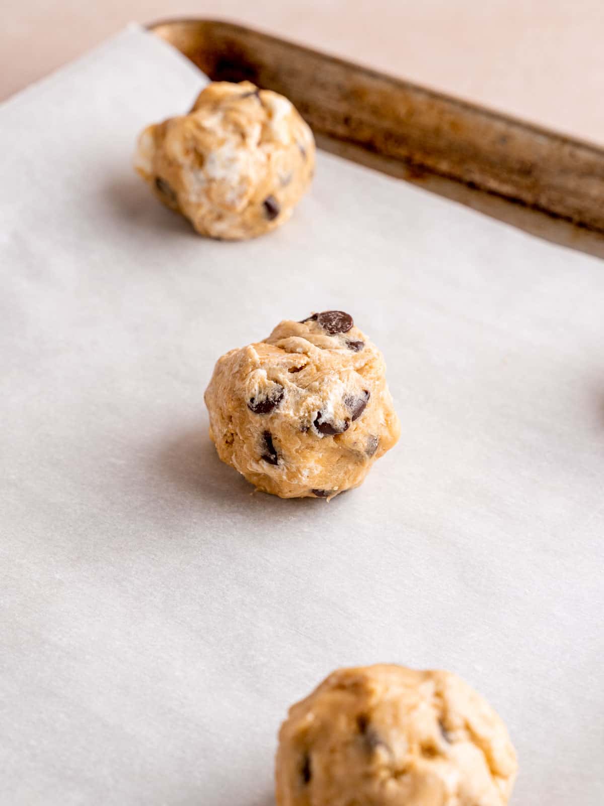 Cookie dough balls on a parchment paper lined baking sheet.