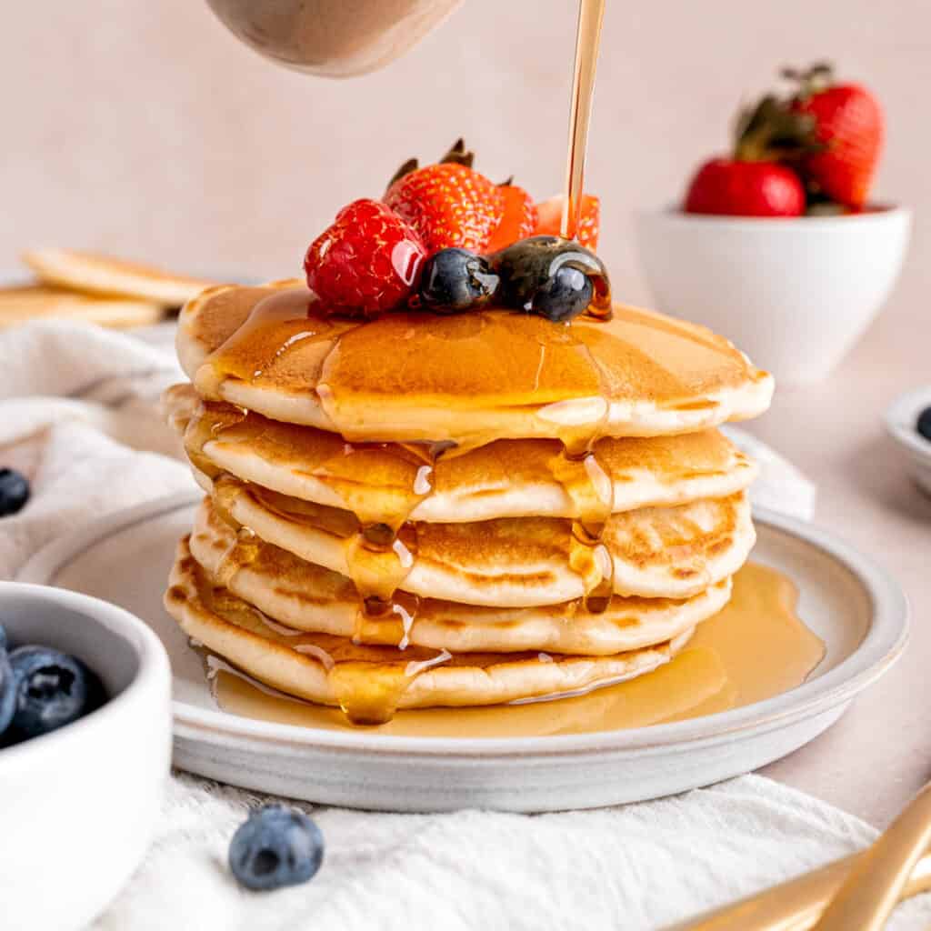 Pouring maple syrup over a stack of sourdough discard pancakes.