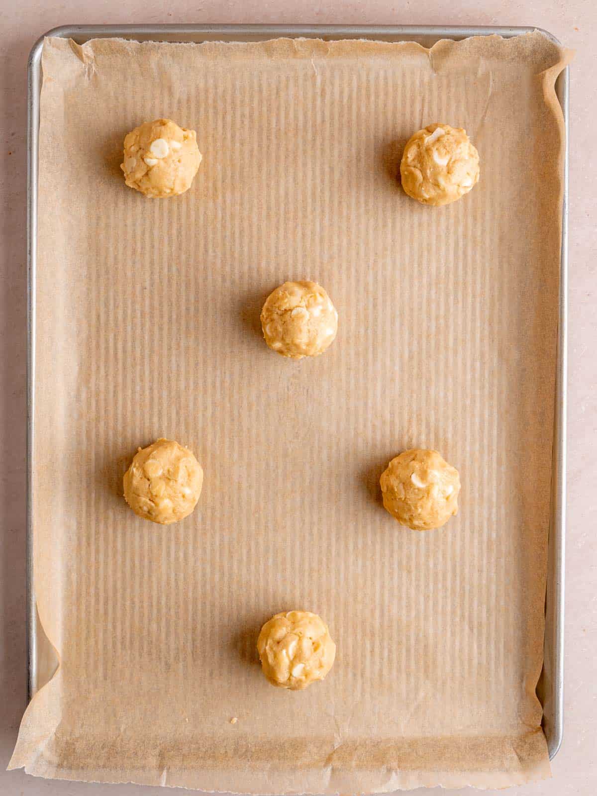 Scoops of white chocolate macadamia cookie dough on a baking sheet.