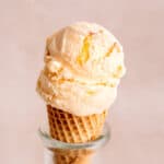 A sugar cone with a scoop of frozen kefir ice cream with fresh peaches.