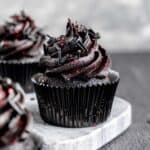 A black velvet cupcake with black cocoa frosting and red and black sprinkles.
