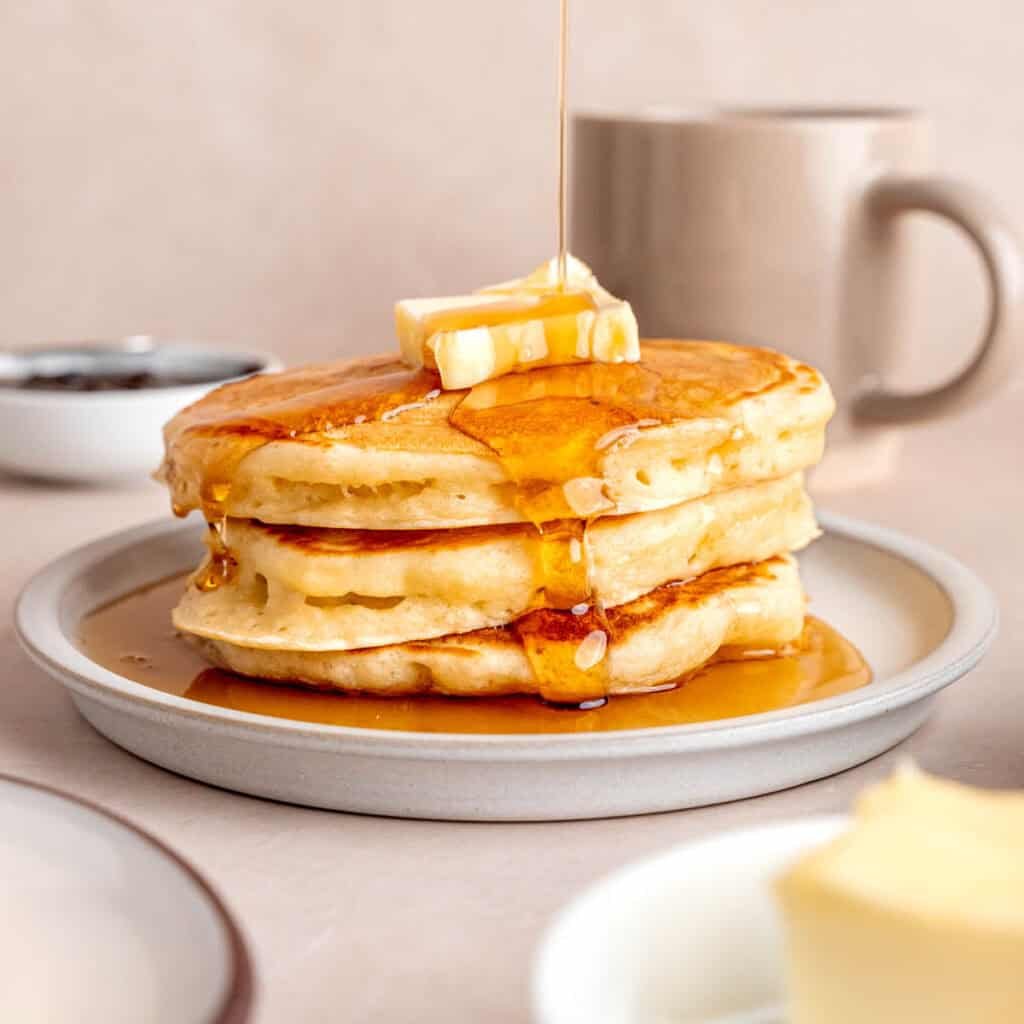 Maple syrup getting poured on top of a stack of kefir pancakes.