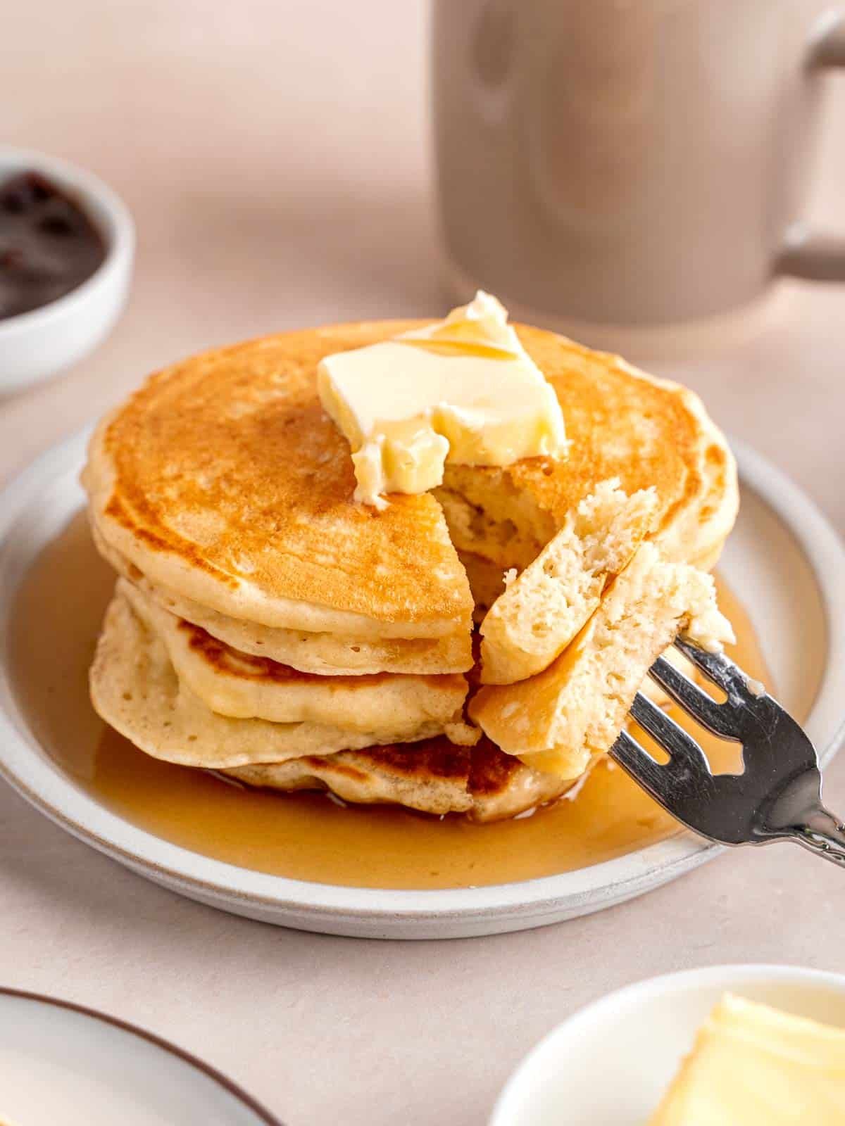 A stack of fluffy kefir pancakes topped with butter and maple syrup.