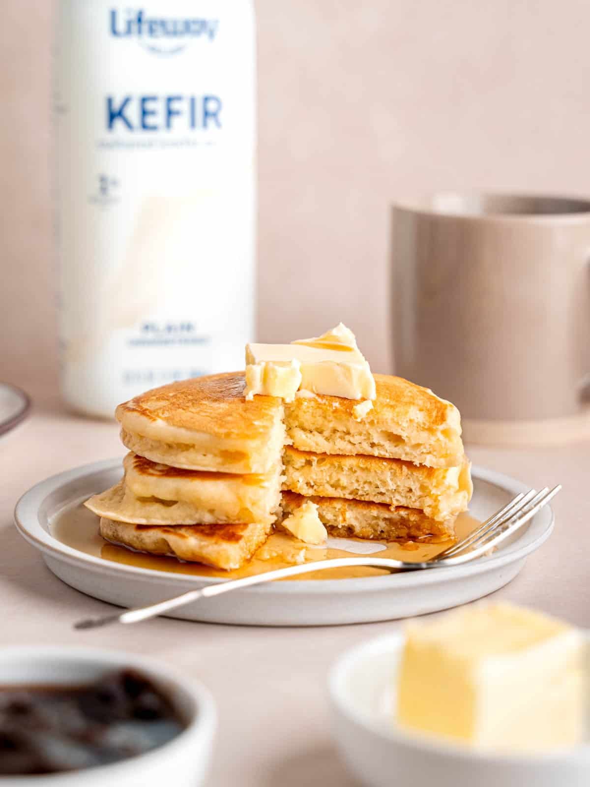 A stack of fluffy pancakes on a plate next to a bottle of Lifeway lowfat kefir.