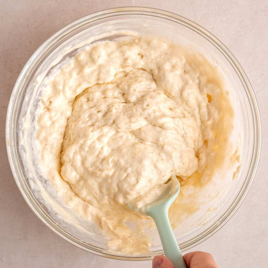 Stirring kefir pancake batter in a bowl with a spatula.
