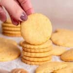 A hand grabbing an orange shortbread cookie from a stack.