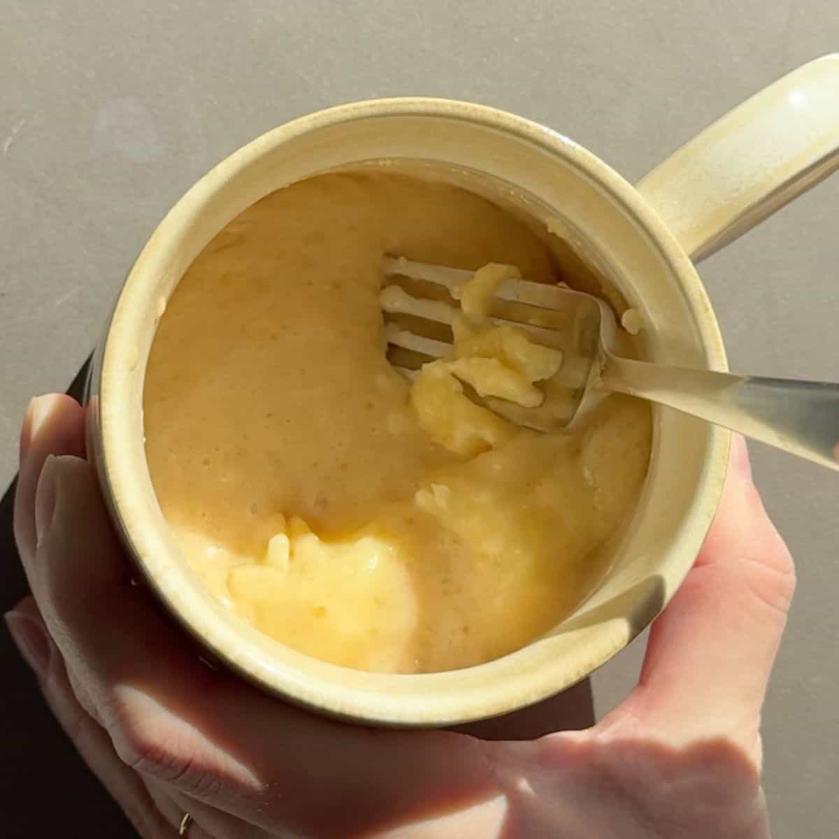 Mashing half of a banana in a coffee mug with wet ingredients.