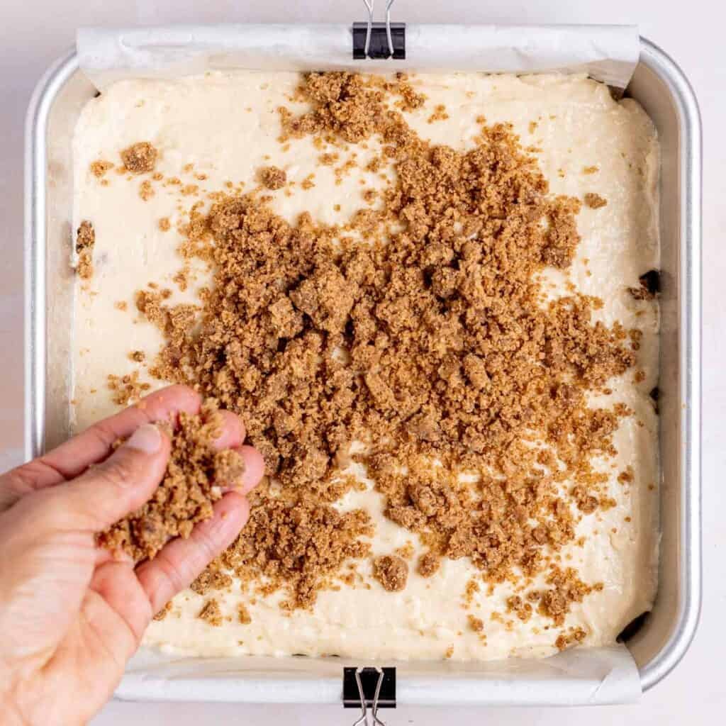 Sprinkling cinnamon crumb topping over a layer of sourdough coffee cake batter.