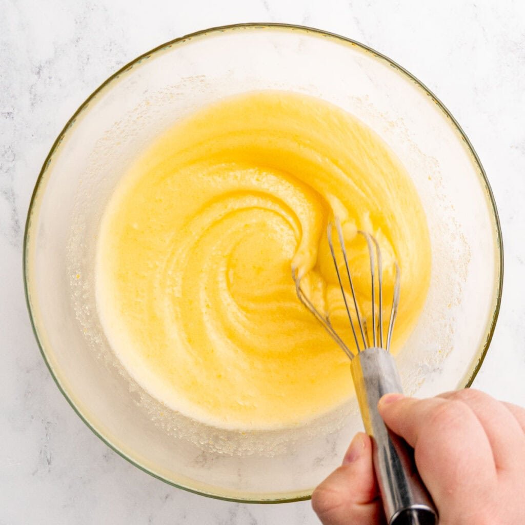 Whisking melted butter, granulated sugar, vanilla extract, and an egg in a bowl.