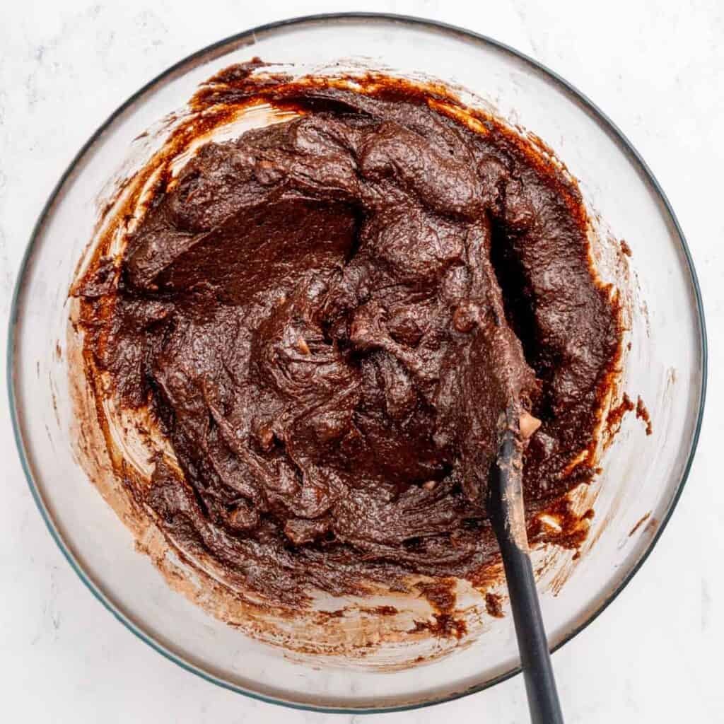 A small batch of brownie batter with chocolate chips in a bowl with a spatula.