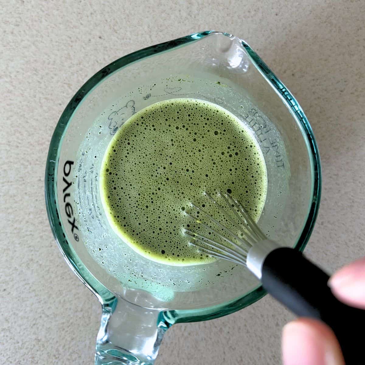 Whisking matcha powder and sugar into warm milk.