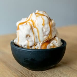 Apple cheesecake ice cream in a bowl with caramel sauce drizzled on top.