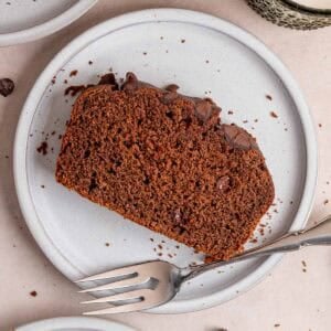 A slice of chocolate loaf cake with chocolate chips on a plate with a fork.