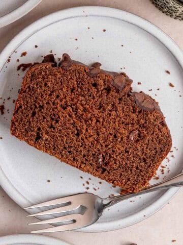 A slice of chocolate loaf cake with chocolate chips on a plate with a fork.