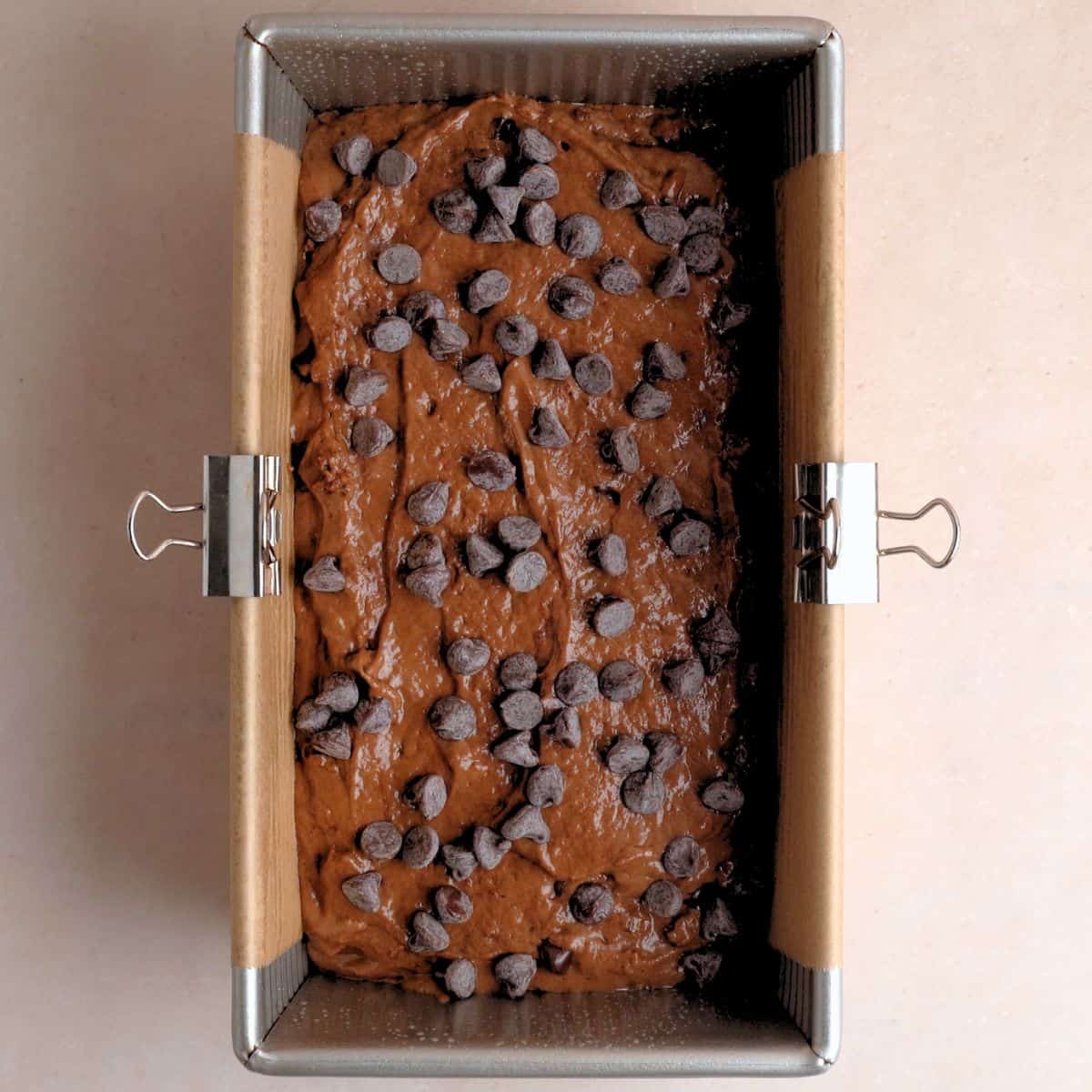 A loaf pan filled with chocolate cake batter sprinkled with chocolate chips.