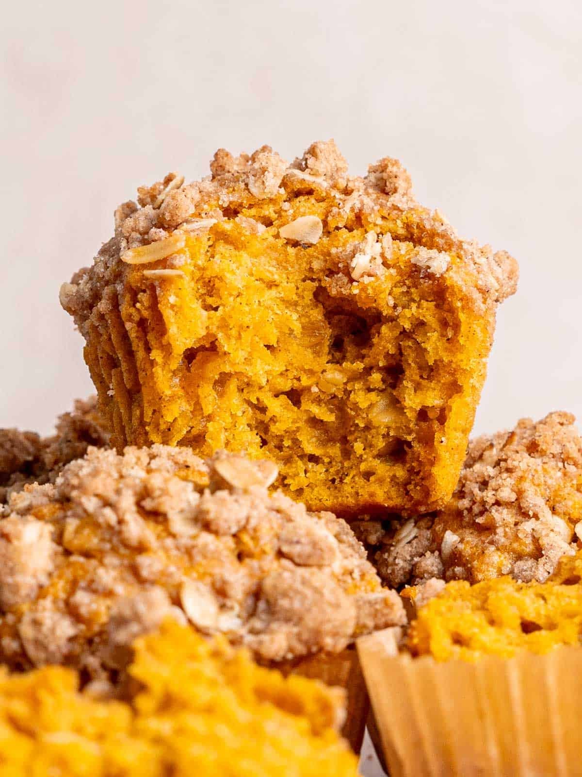 Pumpkin muffins with streusel topping stacked with a bite taken out of one.