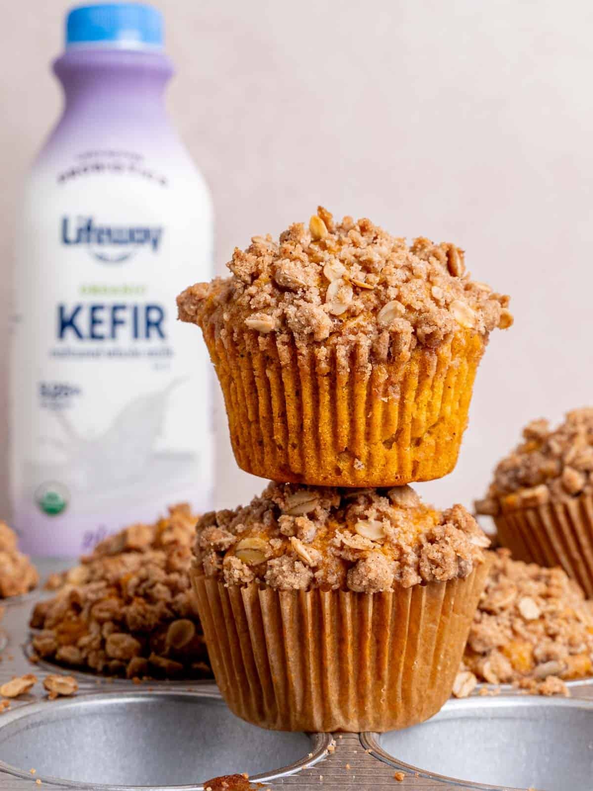 Two pumpkin oatmeal muffins topped with a cinnamon oat streusel topping and a bottle of Lifeway kefir in the back.