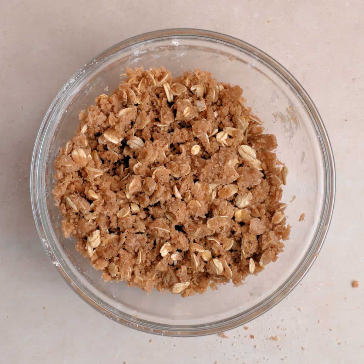 Flour, oats, brown sugar, and cinnamon combined in a bowl with melted butter to resemble a wet sand texture.