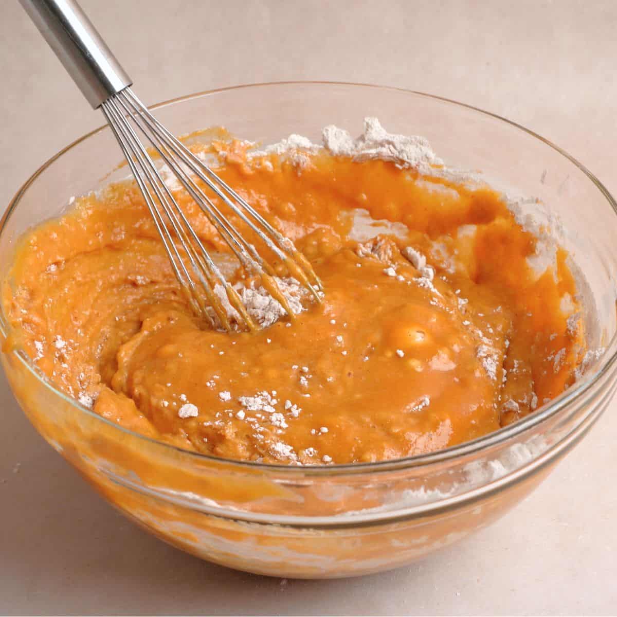 Pumpkin muffin mixture combined in a bowl with a few streaks of flour remaining.