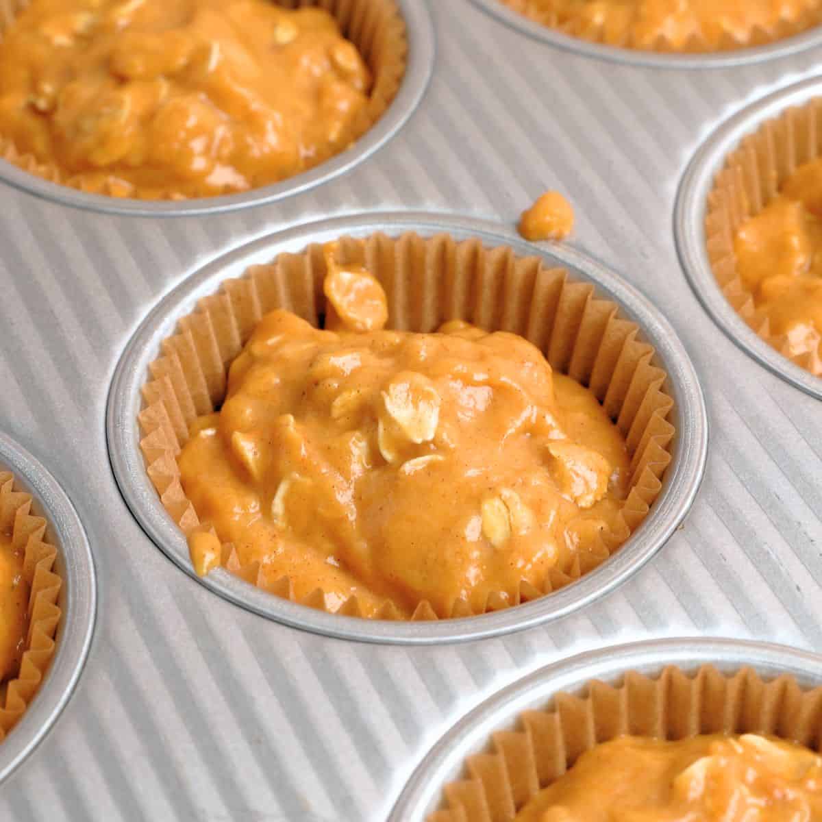 Muffin cups filled ¾ full with pumpkin oatmeal muffin mixture.