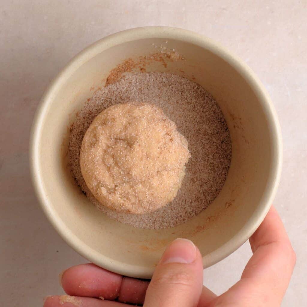 Cookie dough balls being coated in cinnamon & sugar mixture.