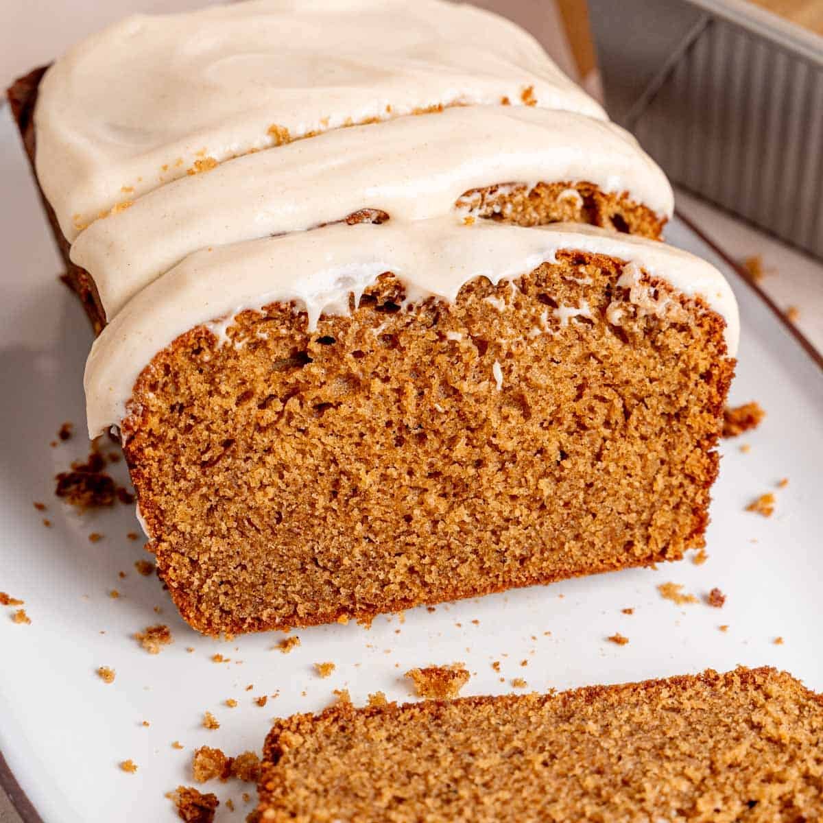 A spice cake loaf cut into slices with cream cheese frosting spread on top.
