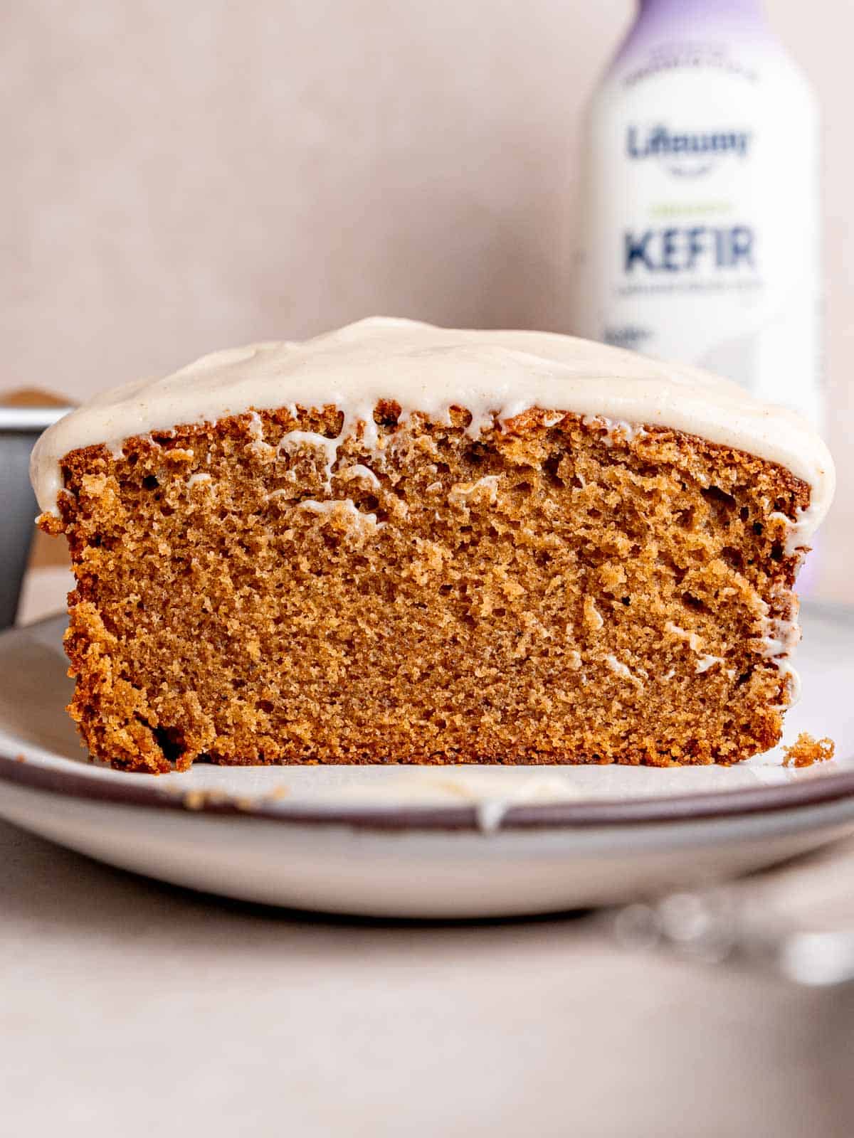 A loaf of spice cake with cream cheese frosting on top sliced down the middle with a bottle of Lifeway kefir in the background.