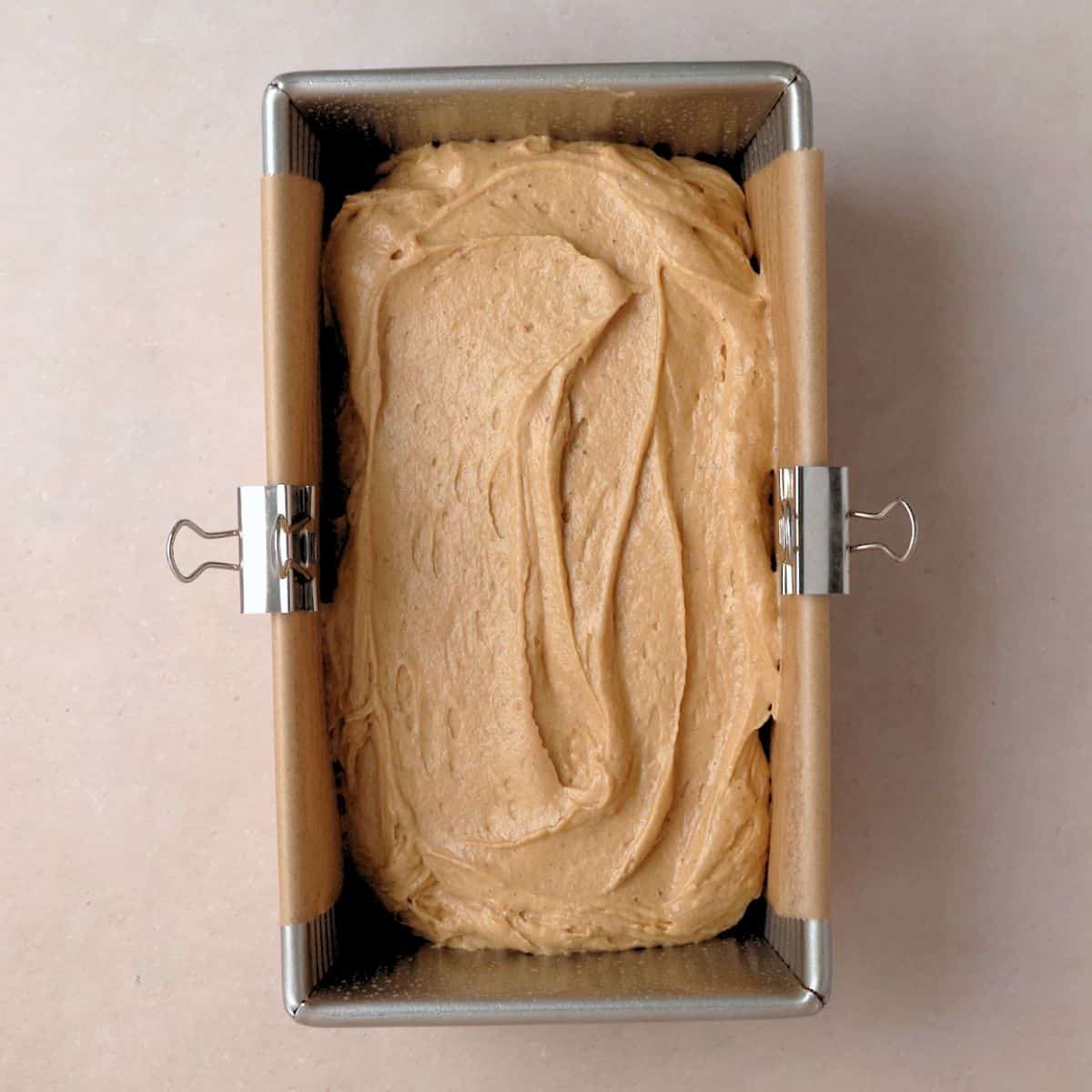 Spice cake batter poured into loaf pan with parchment paper in it.