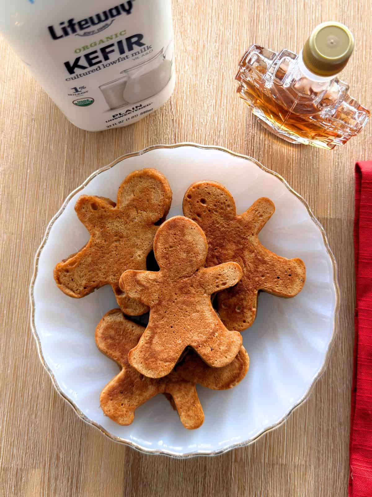 Gingerbread man pancakes on a plate next to bottles of Lifeway kefir and maple syrup.