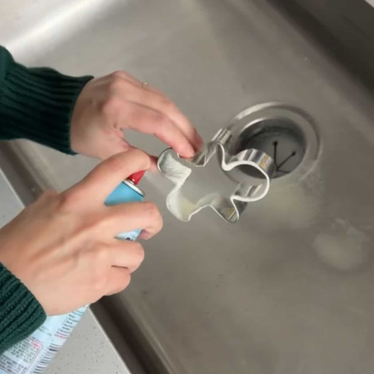 Greasing a metal gingerbread man cookie cutter with nonstick spray.