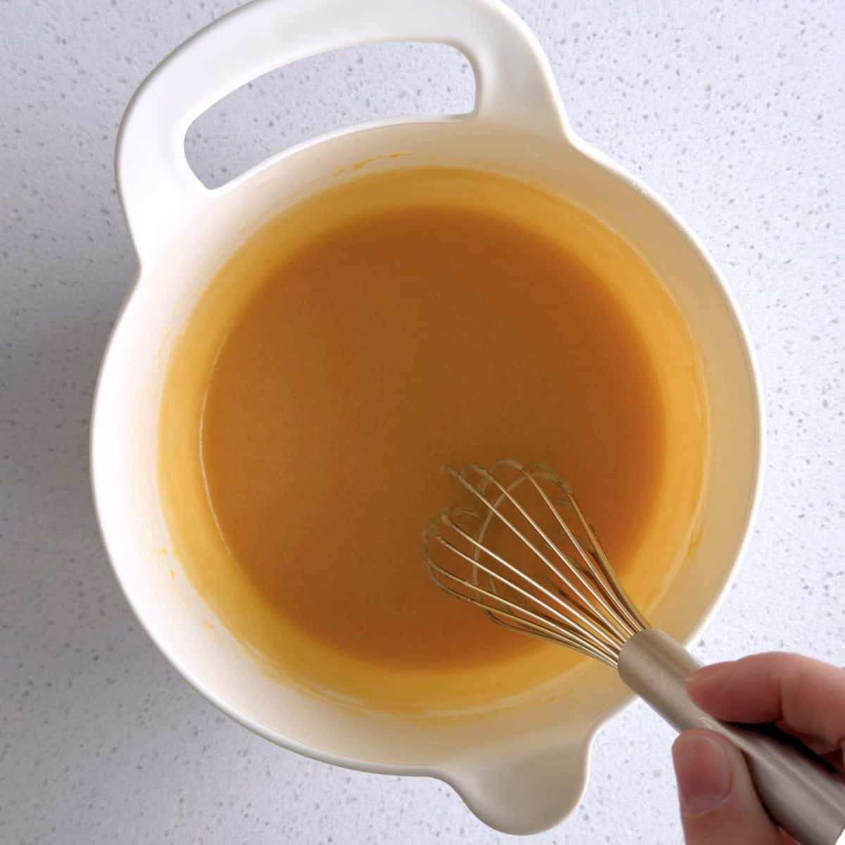 Egg, sugar, honey, vanilla extract, and cooled butter mixed in a bowl.