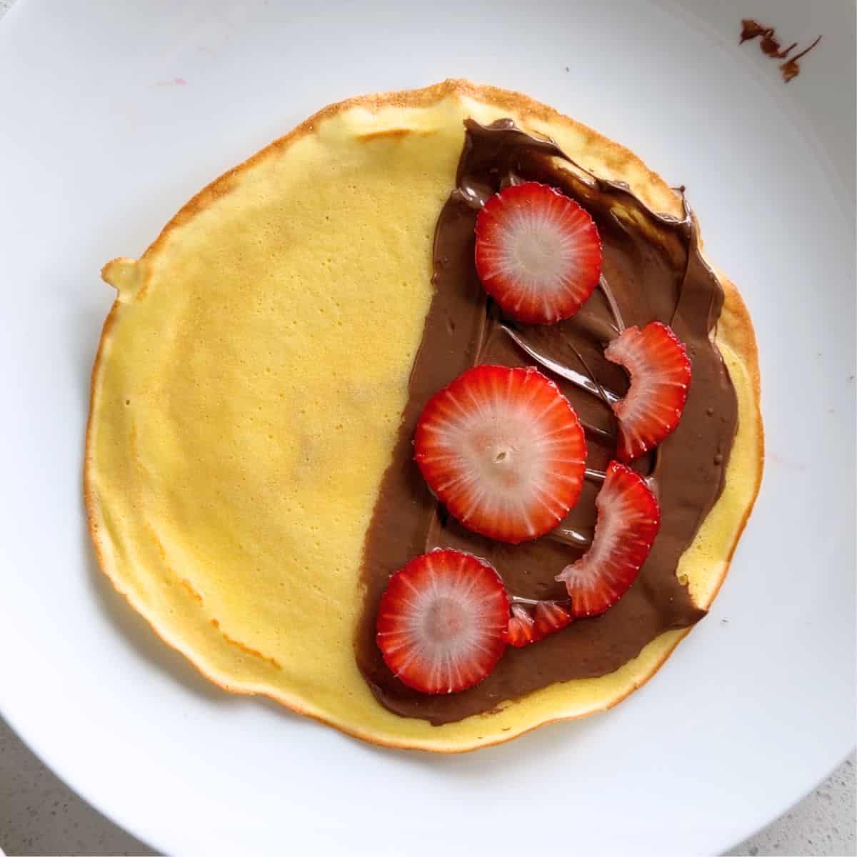 Nutella spread on half of a crepe and topped with strawberry slices.
