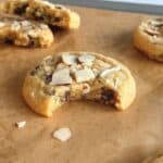 Orange almond chocolate chip cookie on parchment paper with a bite taken out of it.