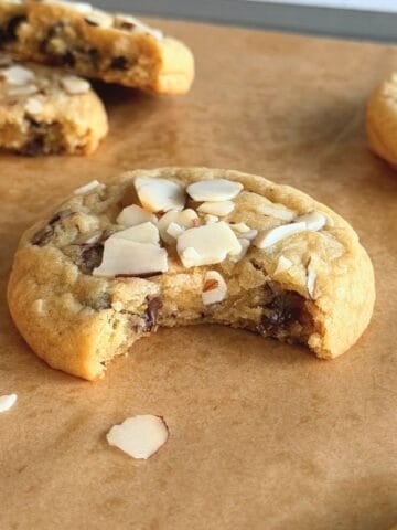 Orange almond chocolate chip cookie on parchment paper with a bite taken out of it.